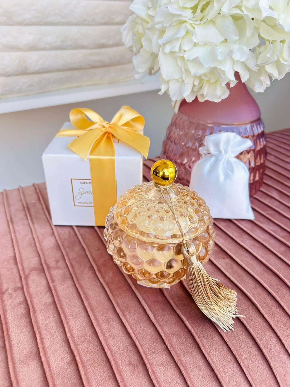 Candela in vetro ambra con forma bon bon e nappina decorativa, firmata Special Gifts, altezza 11 cm, diametro 8 cm, con scatola regalo.